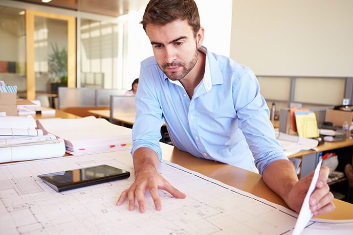 An architect leans on a table while looking at a project blueprint.